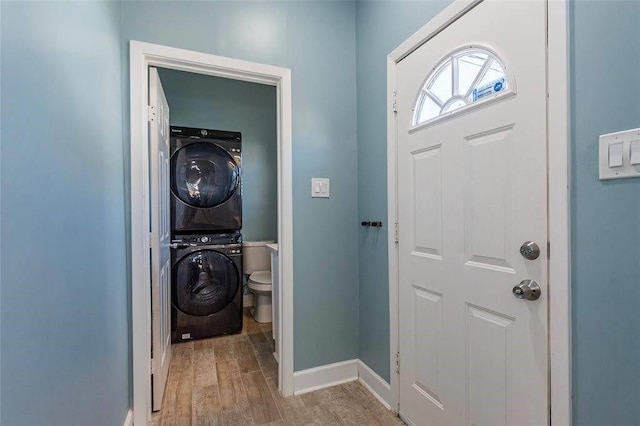 laundry area featuring laundry area, light wood-type flooring, stacked washer / drying machine, and baseboards