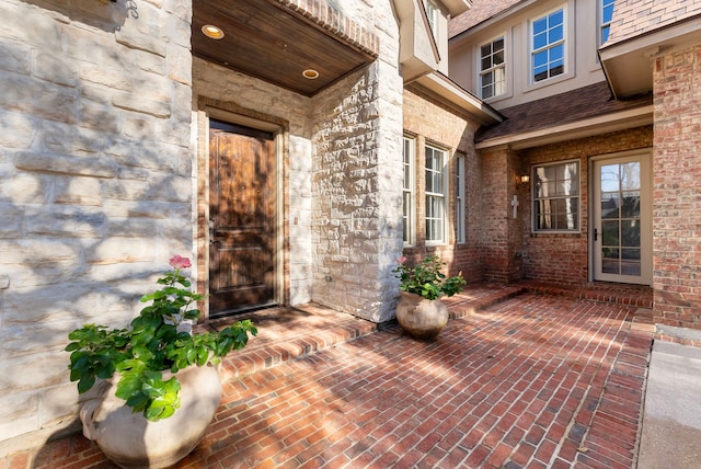 doorway to property featuring brick siding and a shingled roof