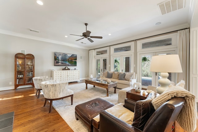 living room featuring visible vents, baseboards, wood finished floors, and crown molding