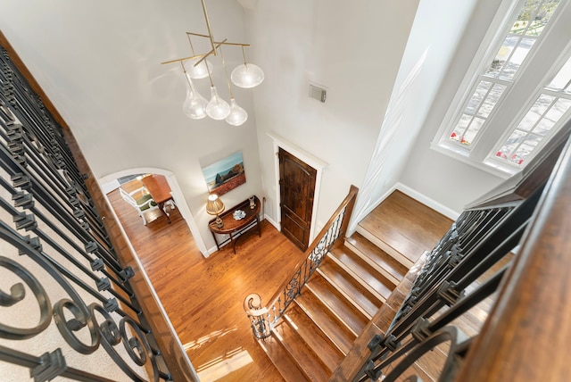 staircase with wood finished floors, visible vents, baseboards, a high ceiling, and arched walkways