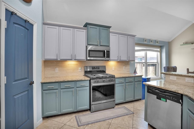 kitchen with light stone countertops, lofted ceiling, light tile patterned flooring, decorative backsplash, and appliances with stainless steel finishes