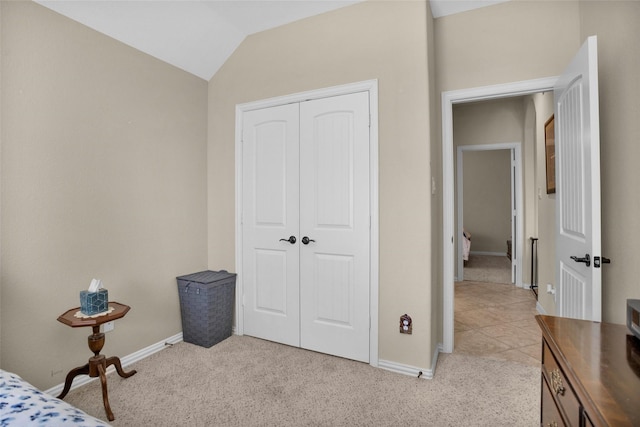 bedroom with a closet, baseboards, light colored carpet, and vaulted ceiling