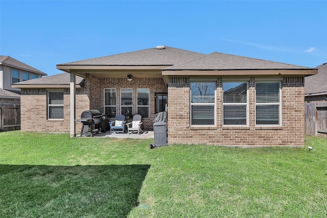 rear view of property featuring fence, a yard, a shingled roof, brick siding, and a patio area