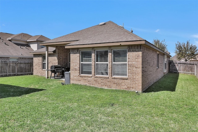 rear view of property featuring a yard, a fenced backyard, brick siding, and roof with shingles