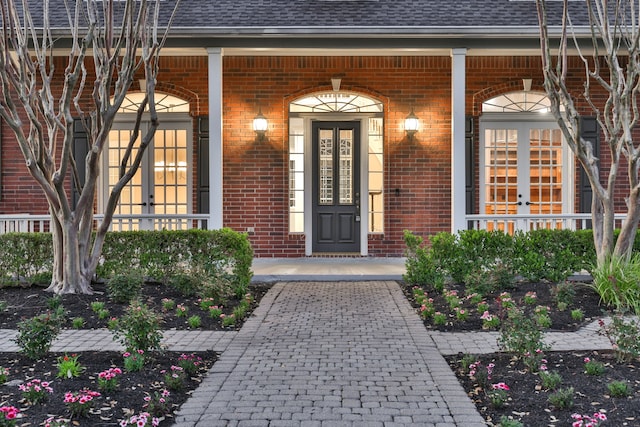 entrance to property with brick siding, a porch, and a shingled roof