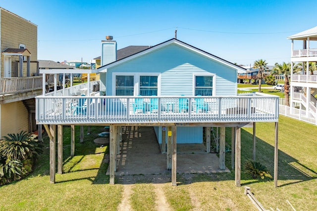 back of property with a wooden deck, a lawn, a chimney, a carport, and driveway