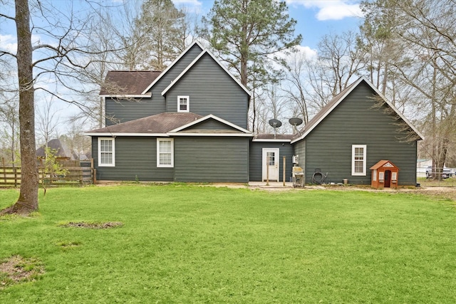 back of property with a lawn, a shingled roof, and fence