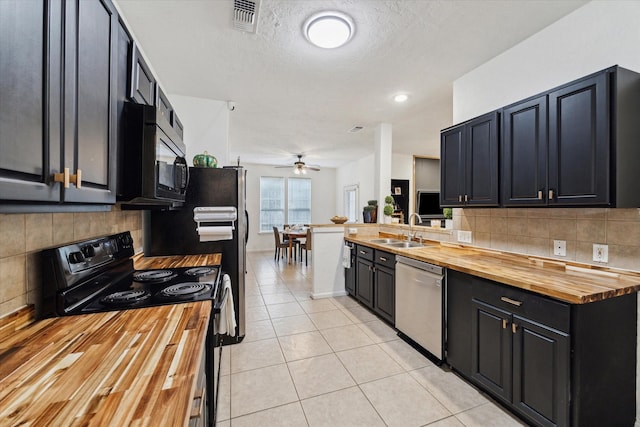 kitchen featuring light tile patterned floors, butcher block counters, black appliances, and a sink