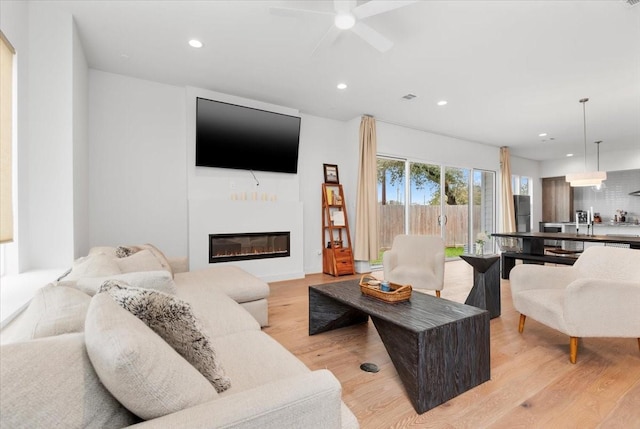 living area with visible vents, light wood-type flooring, recessed lighting, a glass covered fireplace, and a ceiling fan