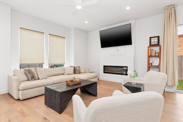 living area with a healthy amount of sunlight, a ceiling fan, light wood finished floors, recessed lighting, and a glass covered fireplace