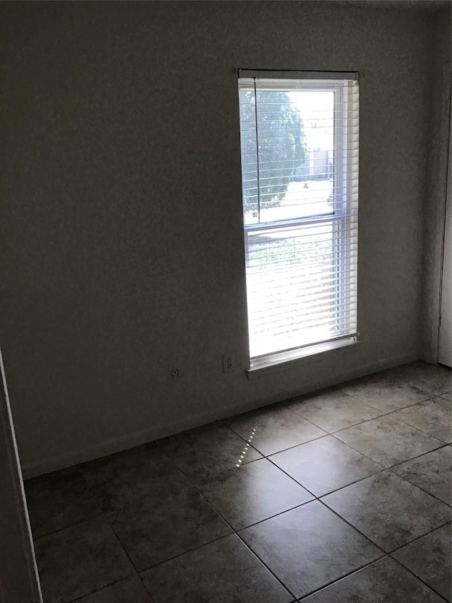 spare room with baseboards, plenty of natural light, and dark tile patterned flooring