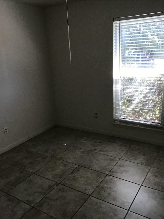 empty room featuring dark tile patterned floors and baseboards