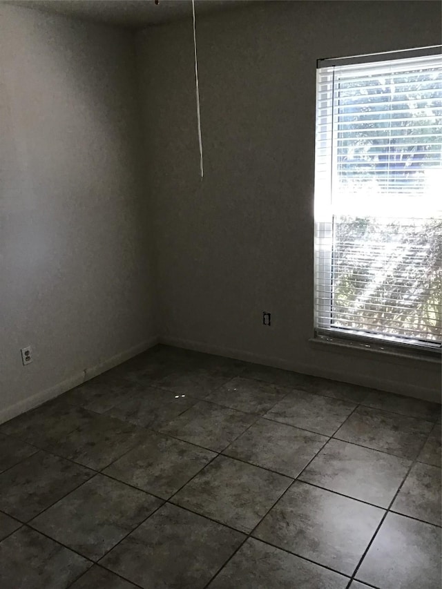 empty room featuring a wealth of natural light, baseboards, and dark tile patterned floors