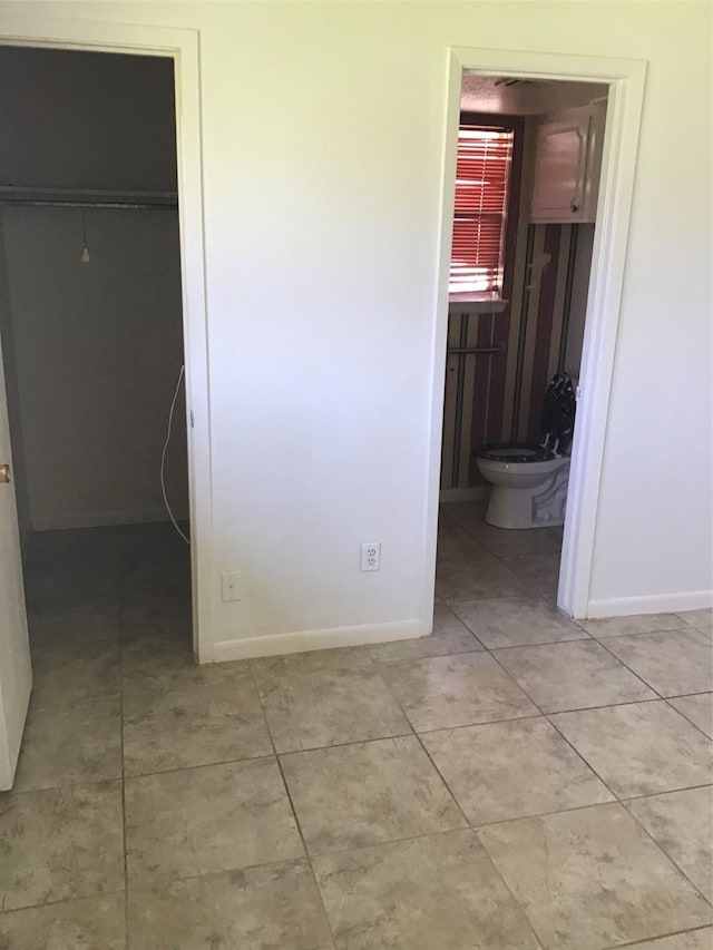 unfurnished bedroom featuring light tile patterned floors, baseboards, a spacious closet, a closet, and connected bathroom