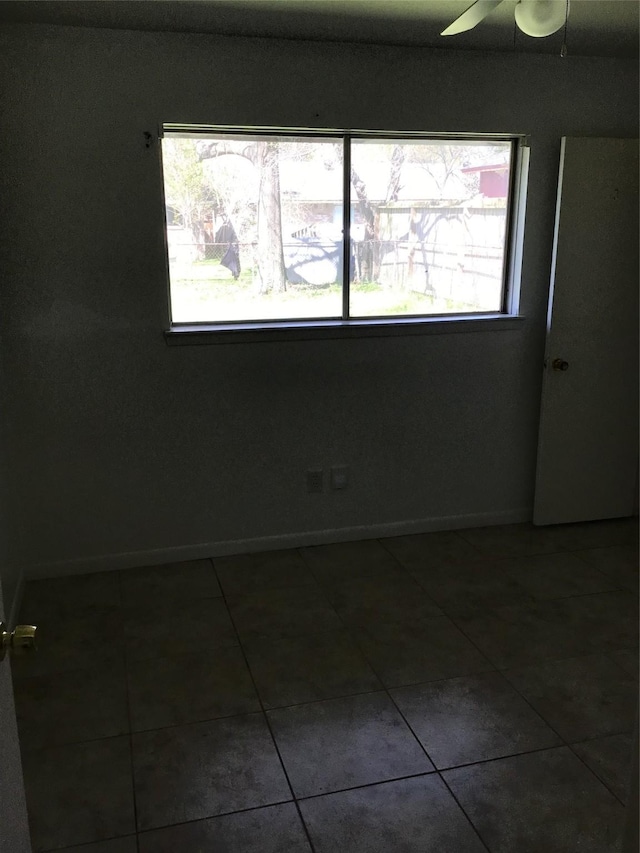 unfurnished room with a ceiling fan, baseboards, and dark tile patterned flooring