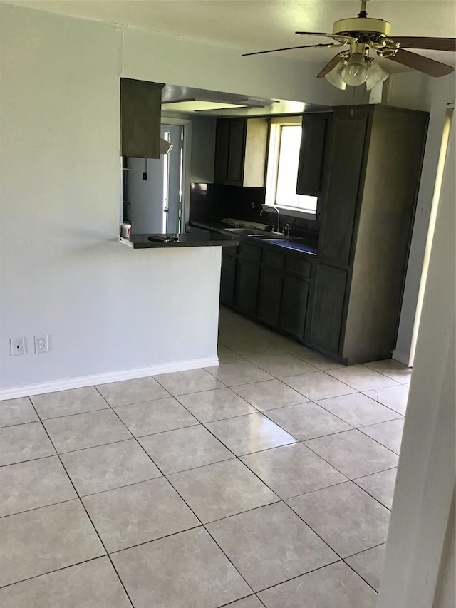 kitchen with dark countertops, light tile patterned floors, a peninsula, dark cabinetry, and a sink