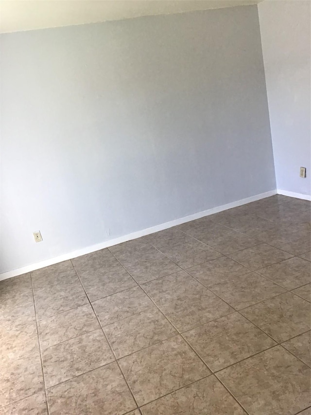 spare room with baseboards and dark tile patterned flooring