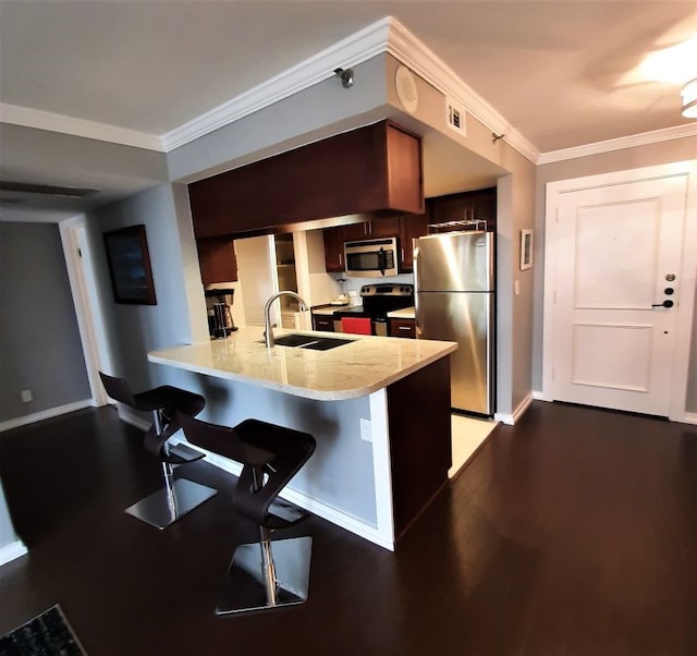 kitchen with crown molding, appliances with stainless steel finishes, a peninsula, wood finished floors, and a sink