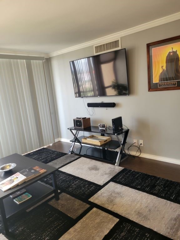 living area featuring crown molding, wood finished floors, visible vents, and baseboards