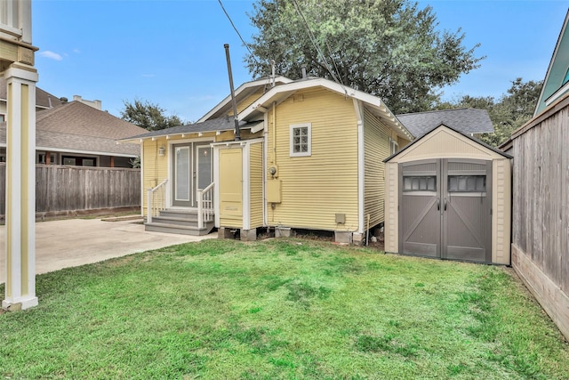 rear view of house featuring a patio, fence, entry steps, a storage unit, and a lawn