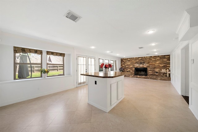 kitchen featuring visible vents, dark countertops, a brick fireplace, open floor plan, and a center island