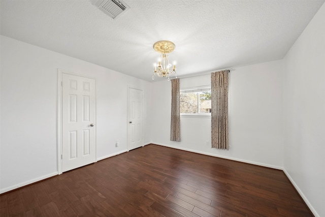 unfurnished room with visible vents, a textured ceiling, wood finished floors, an inviting chandelier, and baseboards