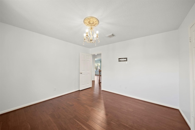 spare room with visible vents, baseboards, an inviting chandelier, and dark wood-style flooring