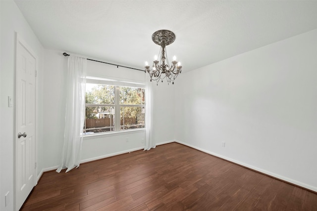 empty room with an inviting chandelier, wood finished floors, and baseboards