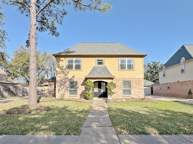 view of front of house featuring a front lawn, fence, brick siding, and a shingled roof