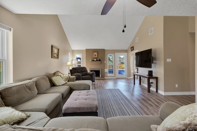 living room featuring ceiling fan, baseboards, a fireplace, wood finished floors, and high vaulted ceiling