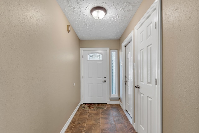 entryway featuring stone finish floor, a textured ceiling, baseboards, and a textured wall