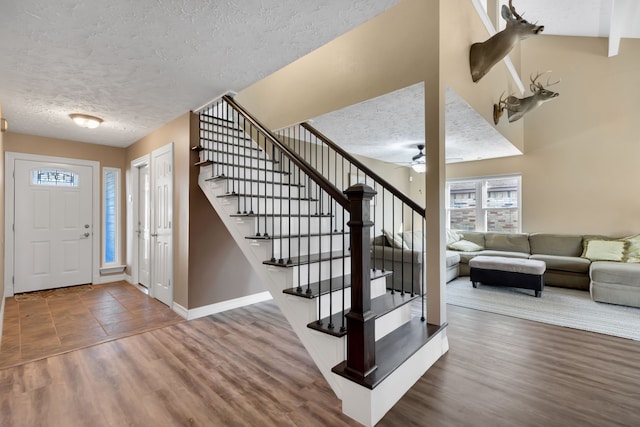 entryway with stairway, a textured ceiling, baseboards, and wood finished floors