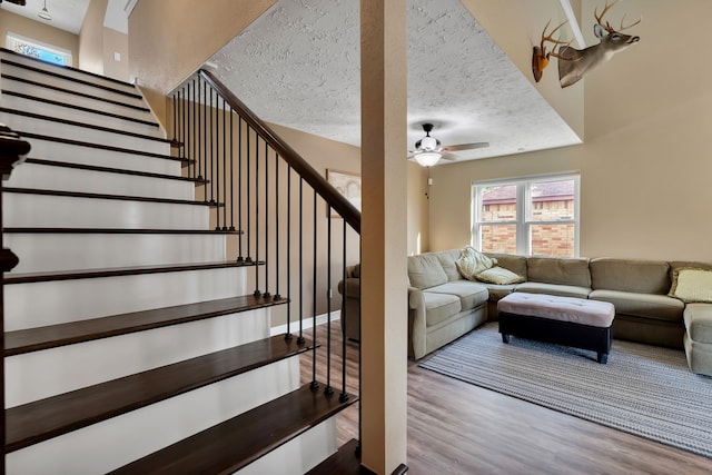 staircase with a textured ceiling, ceiling fan, and wood finished floors