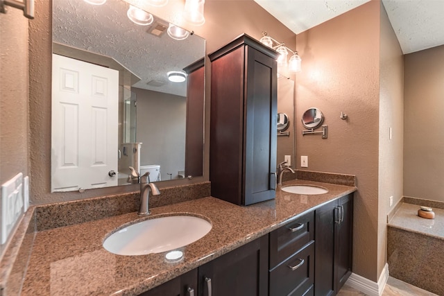 bathroom featuring a textured ceiling, double vanity, toilet, and a sink