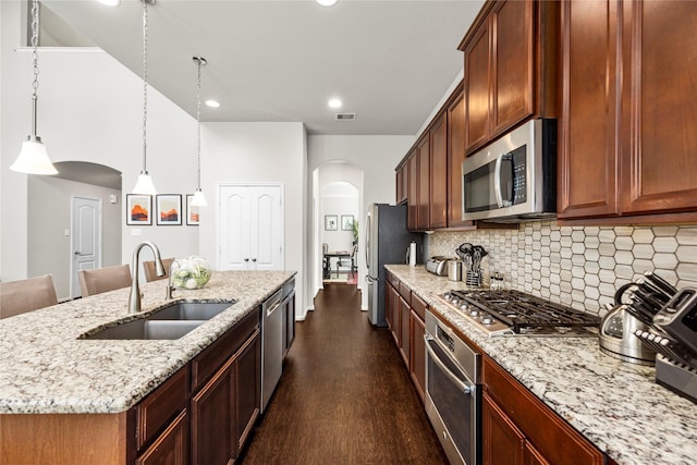 kitchen with arched walkways, stainless steel appliances, a kitchen island with sink, and a sink