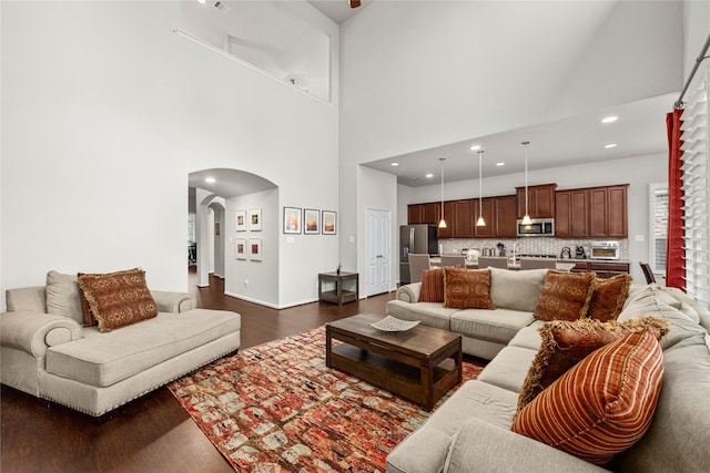 living room with dark wood-style floors, recessed lighting, arched walkways, and a towering ceiling