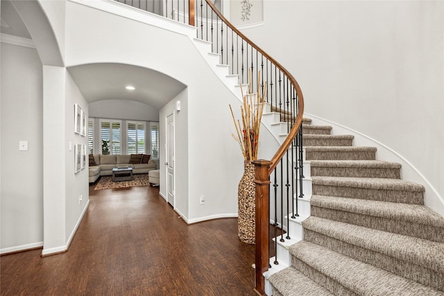 entrance foyer with wood finished floors, baseboards, a high ceiling, arched walkways, and stairs