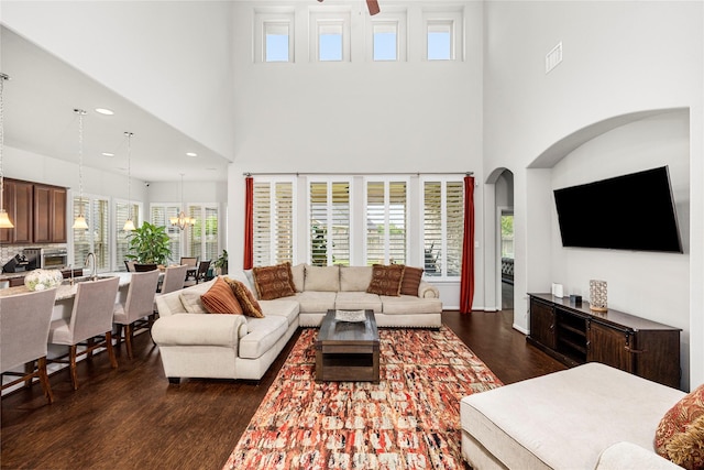 living area with a notable chandelier, a healthy amount of sunlight, a towering ceiling, and dark wood-style flooring