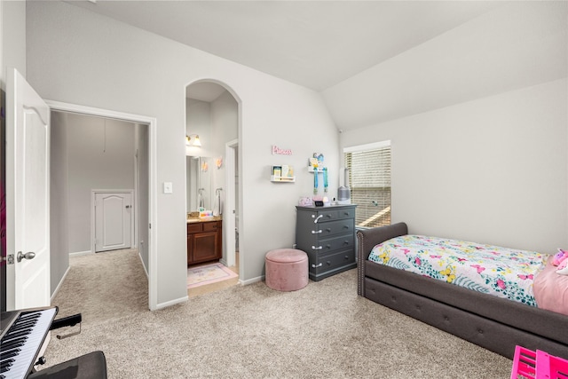 bedroom with baseboards, light colored carpet, vaulted ceiling, arched walkways, and ensuite bath