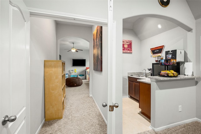 bar featuring light carpet, a ceiling fan, a sink, arched walkways, and baseboards