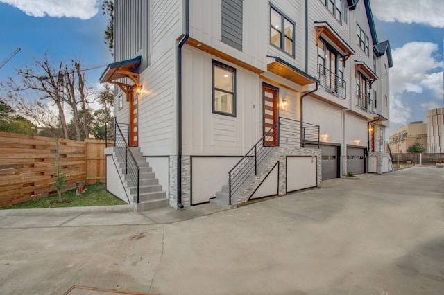 exterior space with stone siding, an attached garage, concrete driveway, and fence