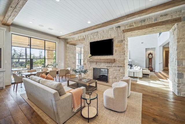 living area featuring a stone fireplace, beam ceiling, hardwood / wood-style flooring, and wooden ceiling