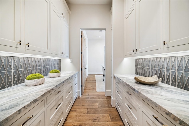 kitchen with white cabinets, light wood-style floors, baseboards, and backsplash