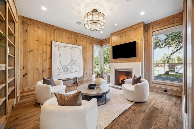 living room with hardwood / wood-style floors, wooden walls, a fireplace with flush hearth, and visible vents