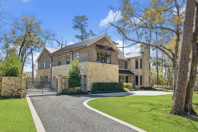 view of front of home with gravel driveway, a front lawn, fence, metal roof, and stone siding