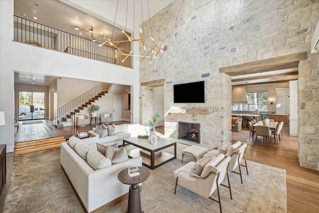 living area featuring visible vents, a stone fireplace, hardwood / wood-style flooring, stairs, and a notable chandelier