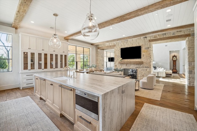 kitchen with a stone fireplace, beam ceiling, light wood-type flooring, and a sink