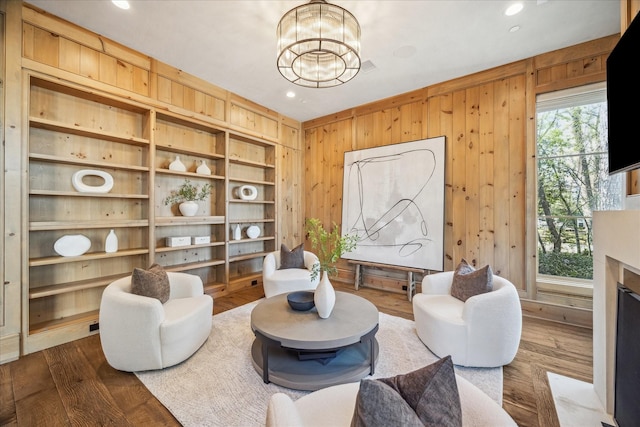 sitting room with a fireplace with flush hearth, a notable chandelier, dark wood-type flooring, recessed lighting, and wood walls