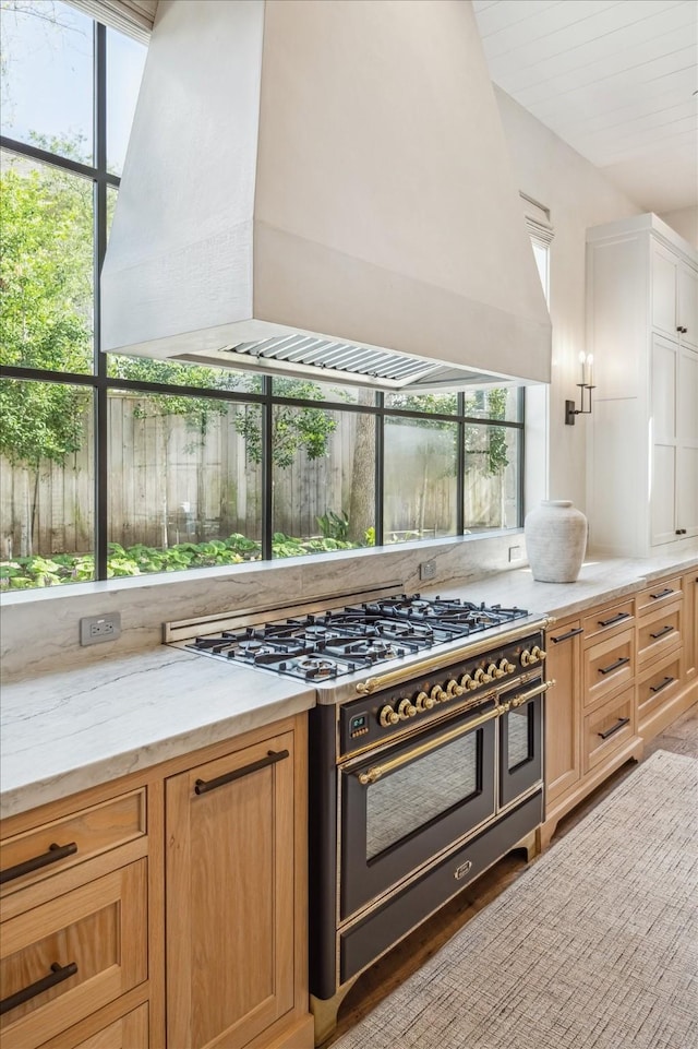 kitchen featuring white cabinetry, custom exhaust hood, range with two ovens, and light stone counters