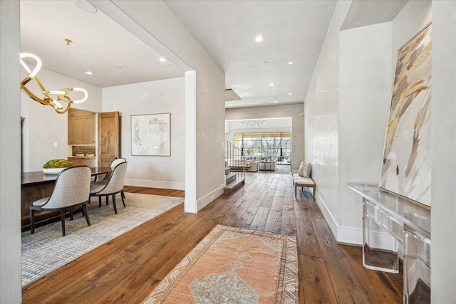 hall featuring hardwood / wood-style flooring, recessed lighting, an inviting chandelier, baseboards, and stairs